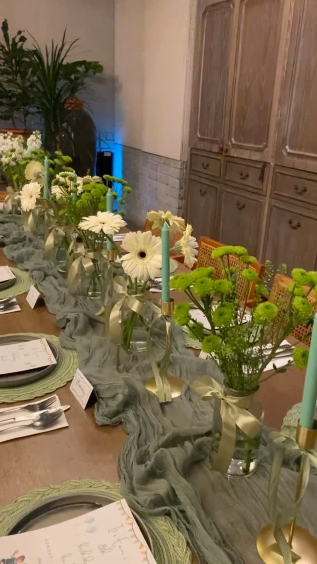 A long wedding table featuring sage green runners, white flowers, and light green candles.