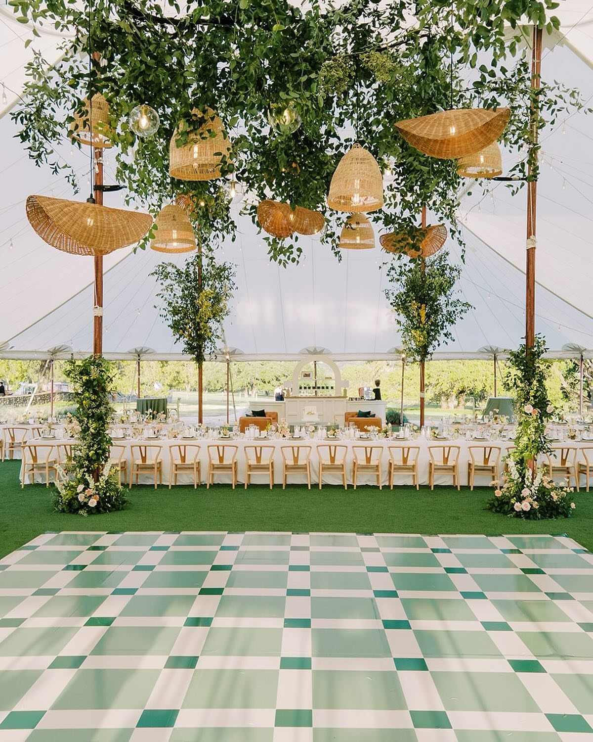 Checkered sage green and white dance floor inside a decorated wedding tent.