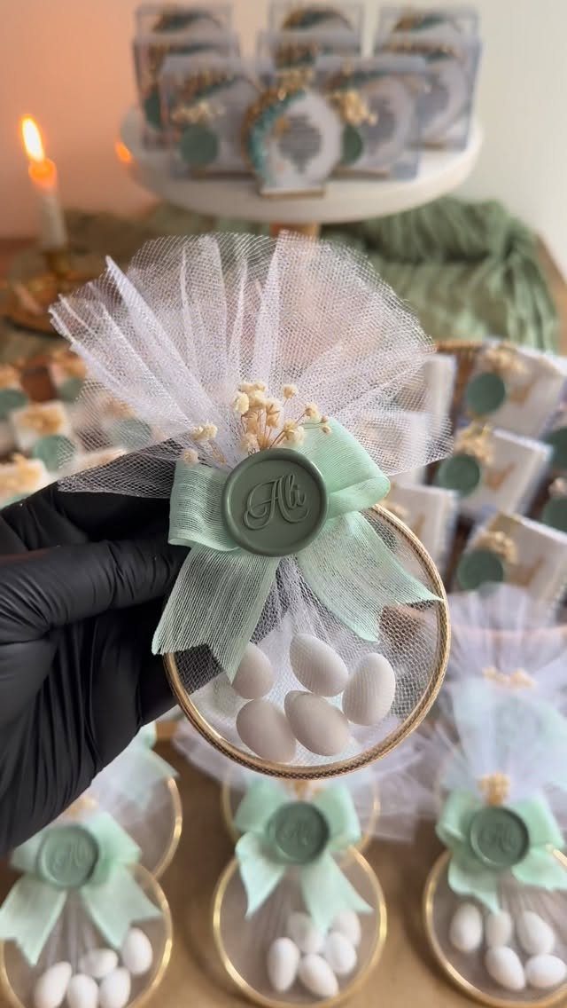 A sage green wedding favor containing white almonds, tulle, and a decorative ribbon.