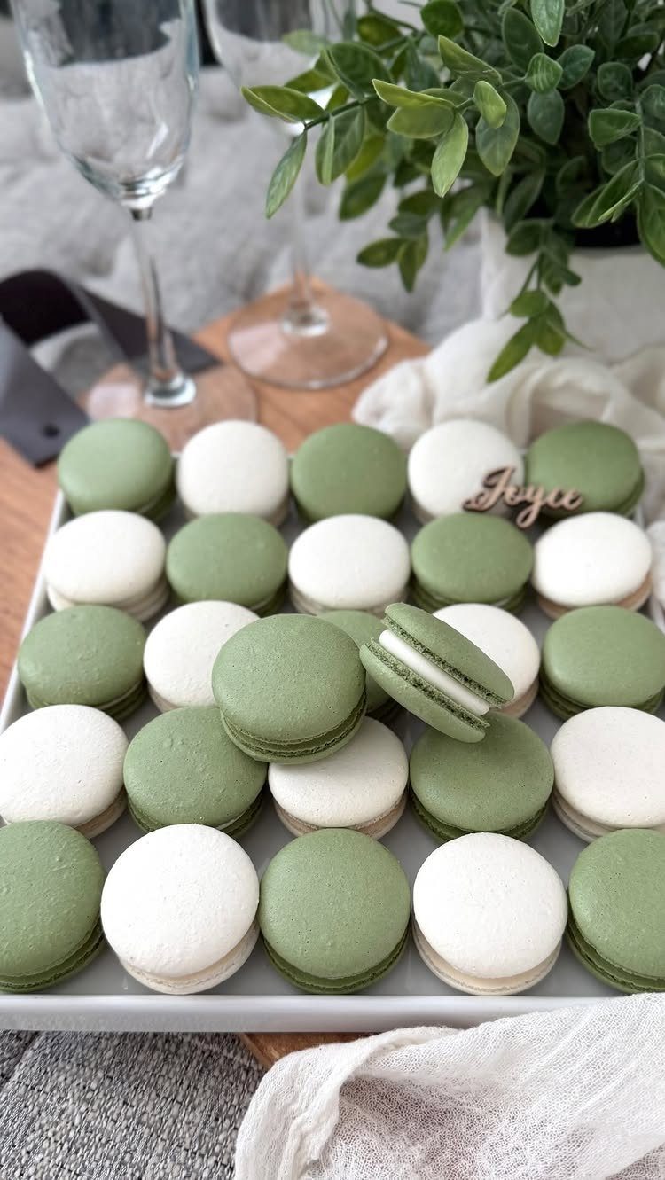 Sage green and white macarons arranged neatly on a white rectangular serving tray.