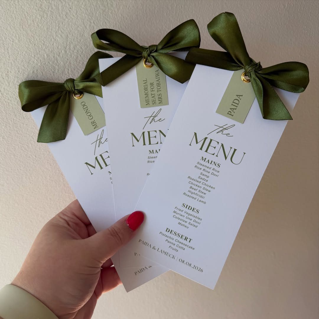 Hand holding three white wedding menus decorated with sage green bows and name tags.