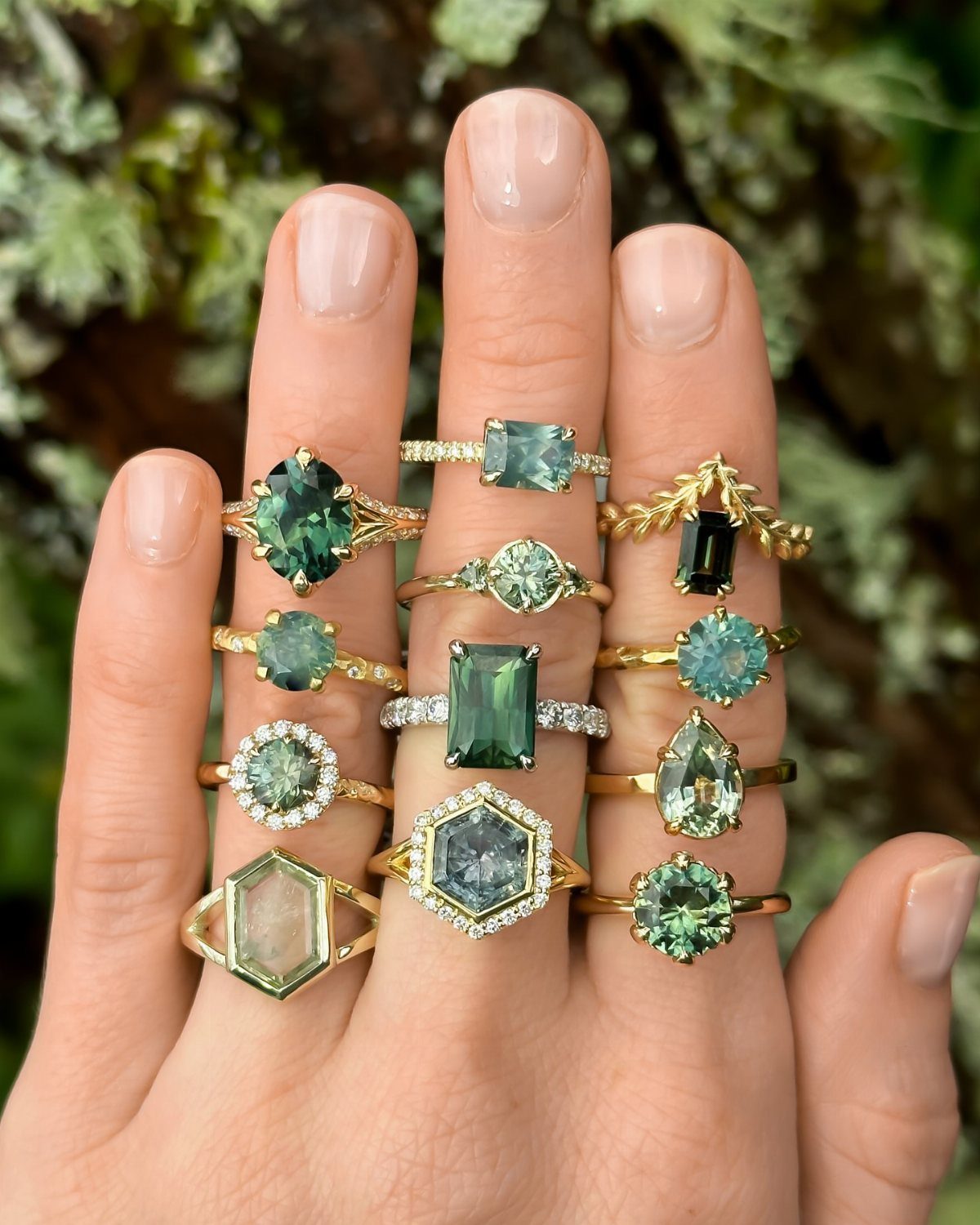 A hand adorned with multiple gold rings featuring various sage green gemstones.