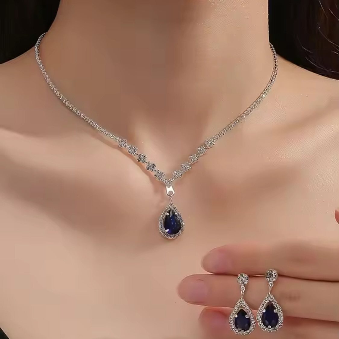 Silver necklace and earrings featuring teardrop-shaped blue gemstones worn by a person.