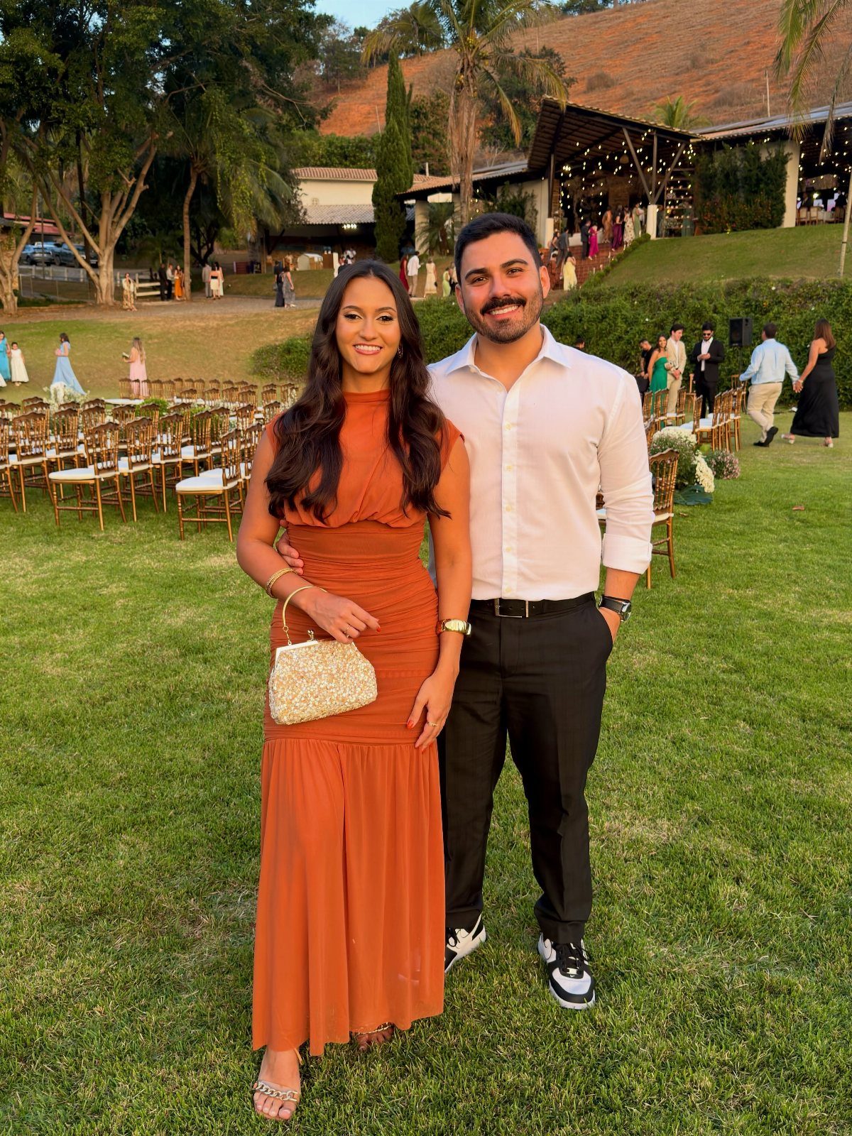 A man in a white shirt and a woman in a rust maxi dress posing on grass.