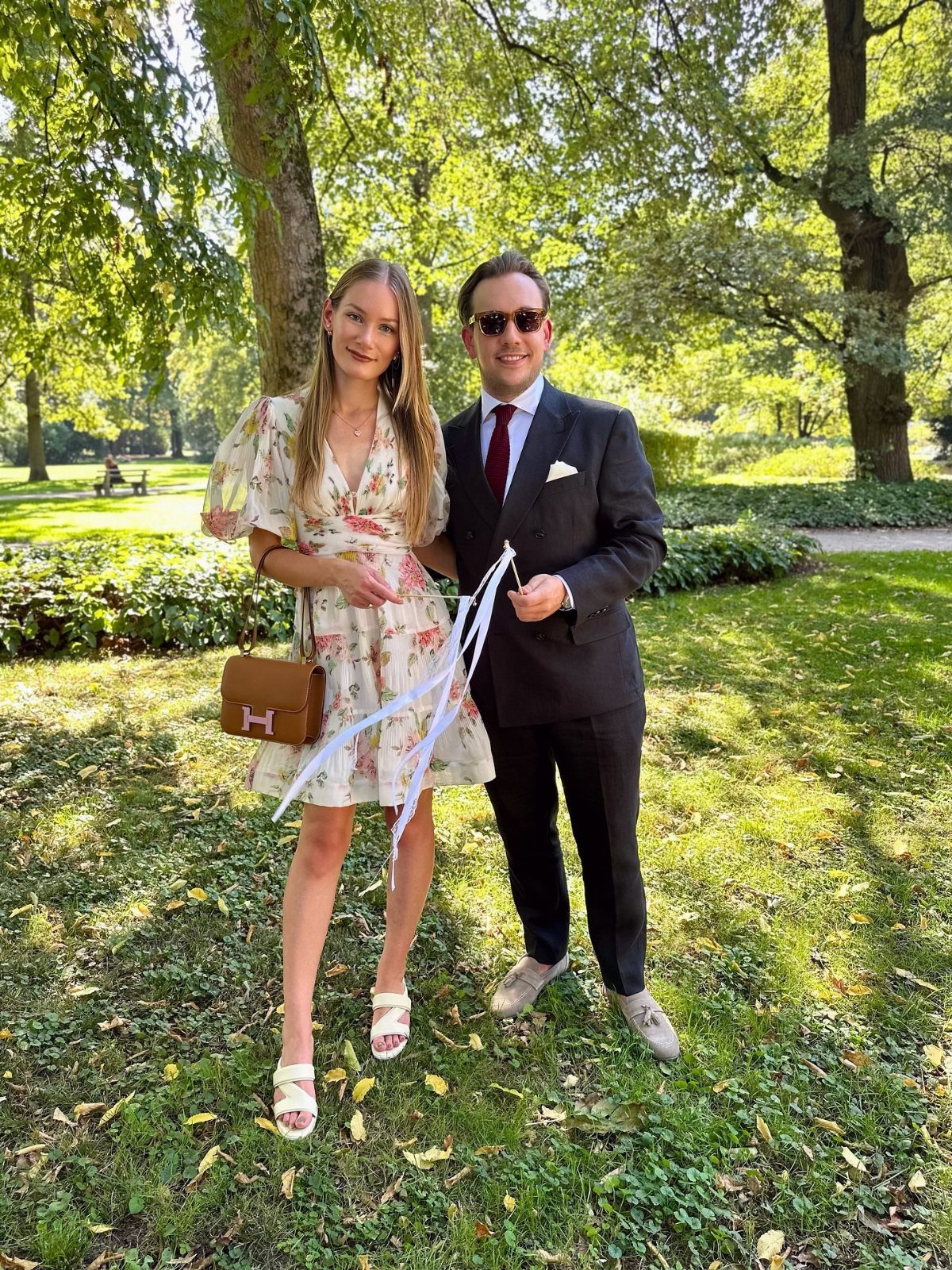 A woman in a floral dress and a man in a dark suit posing in a park.