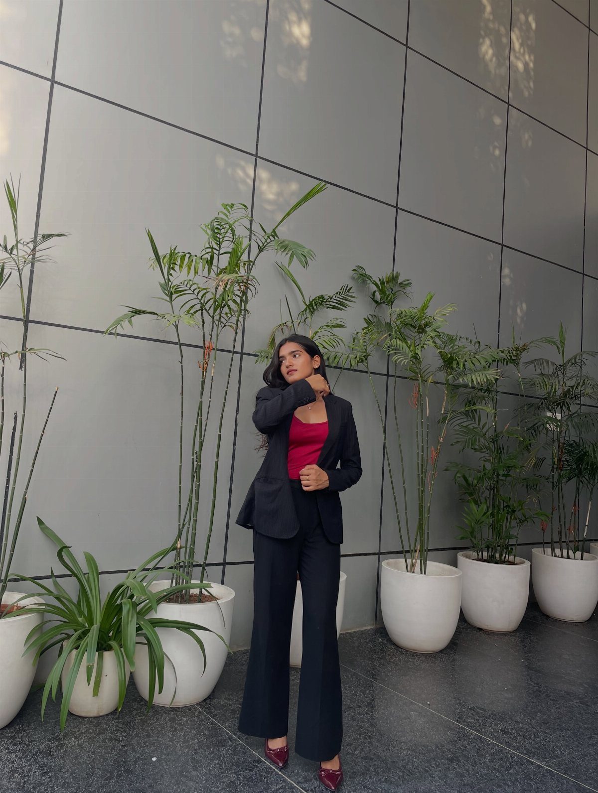 Woman posing in a navy blue pantsuit and red top among potted palm plants.