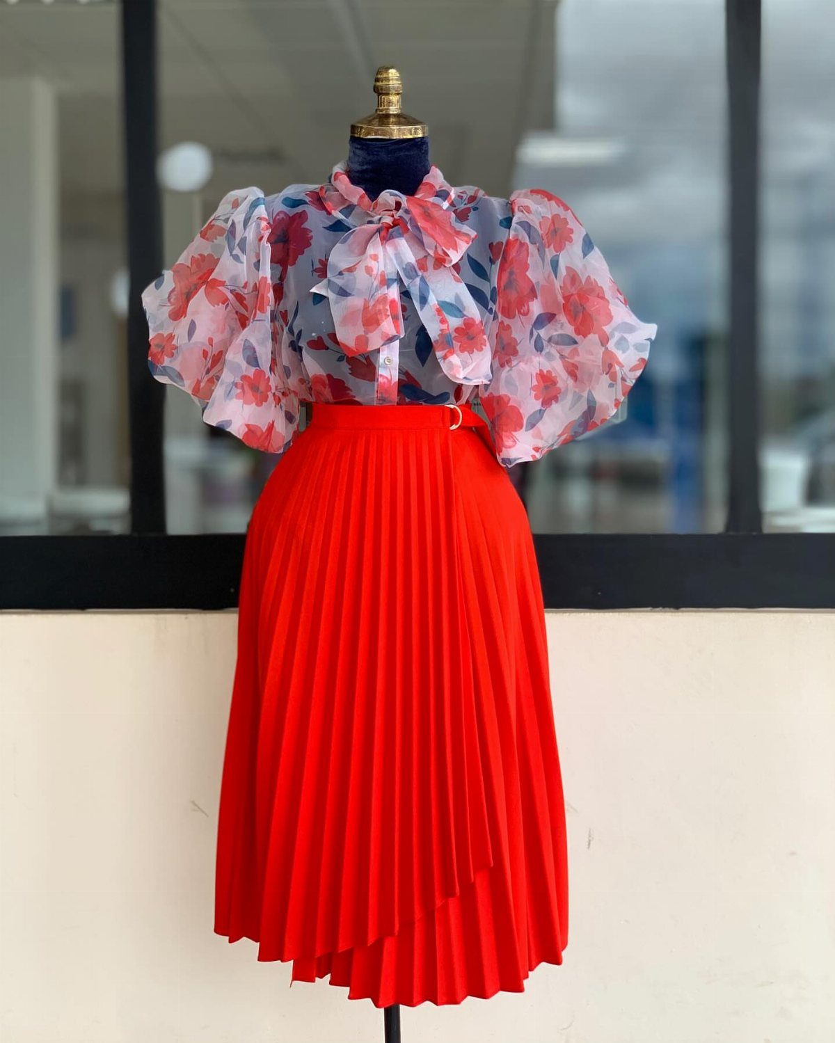 A floral puff-sleeve blouse and bright red pleated skirt displayed on a mannequin.