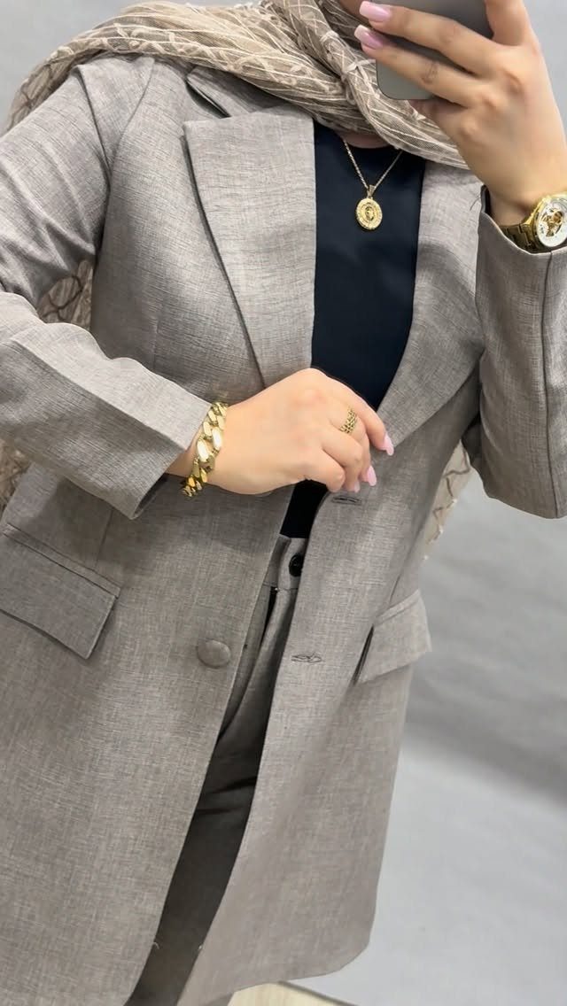 Person wearing a grey textured blazer, black top, and gold jewelry accessories.