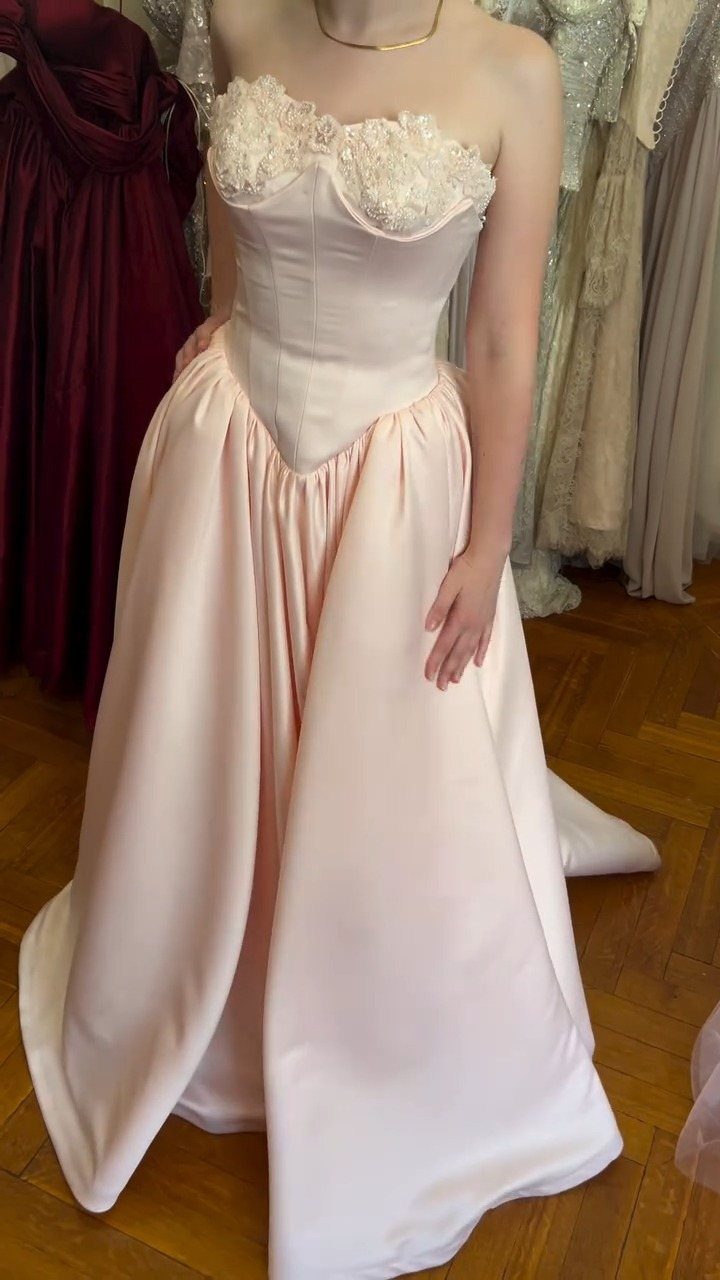 A person wearing a pale pink strapless satin gown with a lace corset bodice.