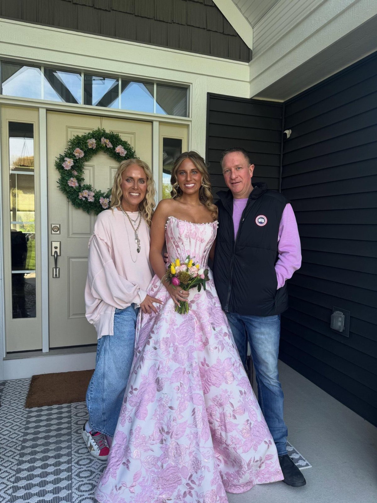 Young woman wearing a pink floral print strapless ballgown holding a small bouquet of flowers.