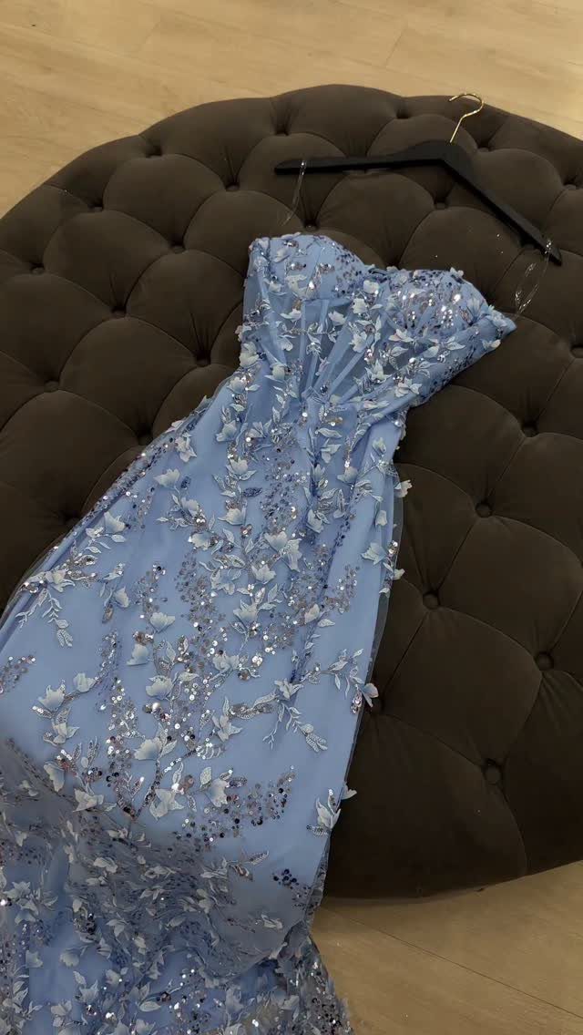 Light blue strapless formal gown with silver sequins and 3D floral appliqués on a tufted ottoman.