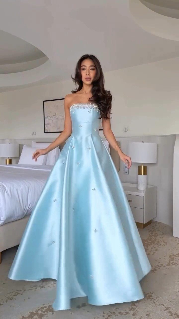 A woman wearing a light blue strapless A-line satin gown in a bedroom.