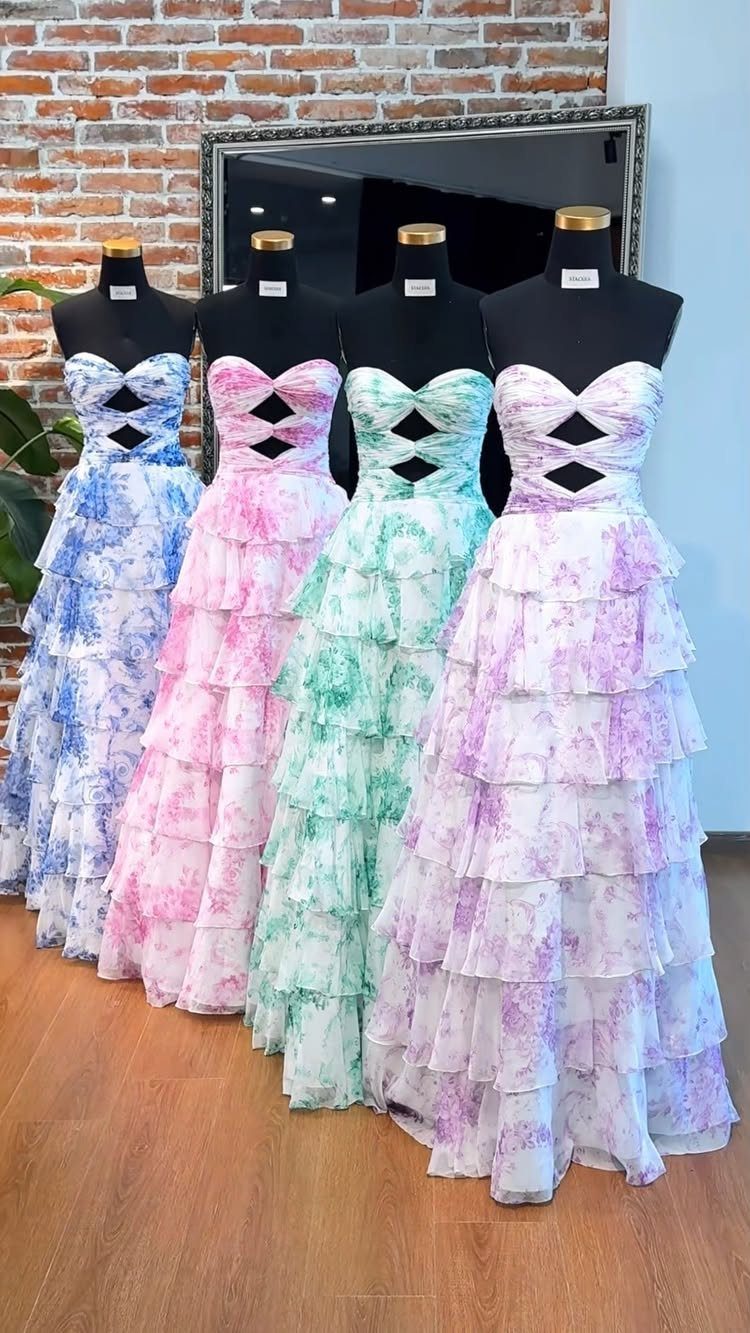 Four mannequins wearing colorful floral tiered ruffled prom dresses against a brick wall.