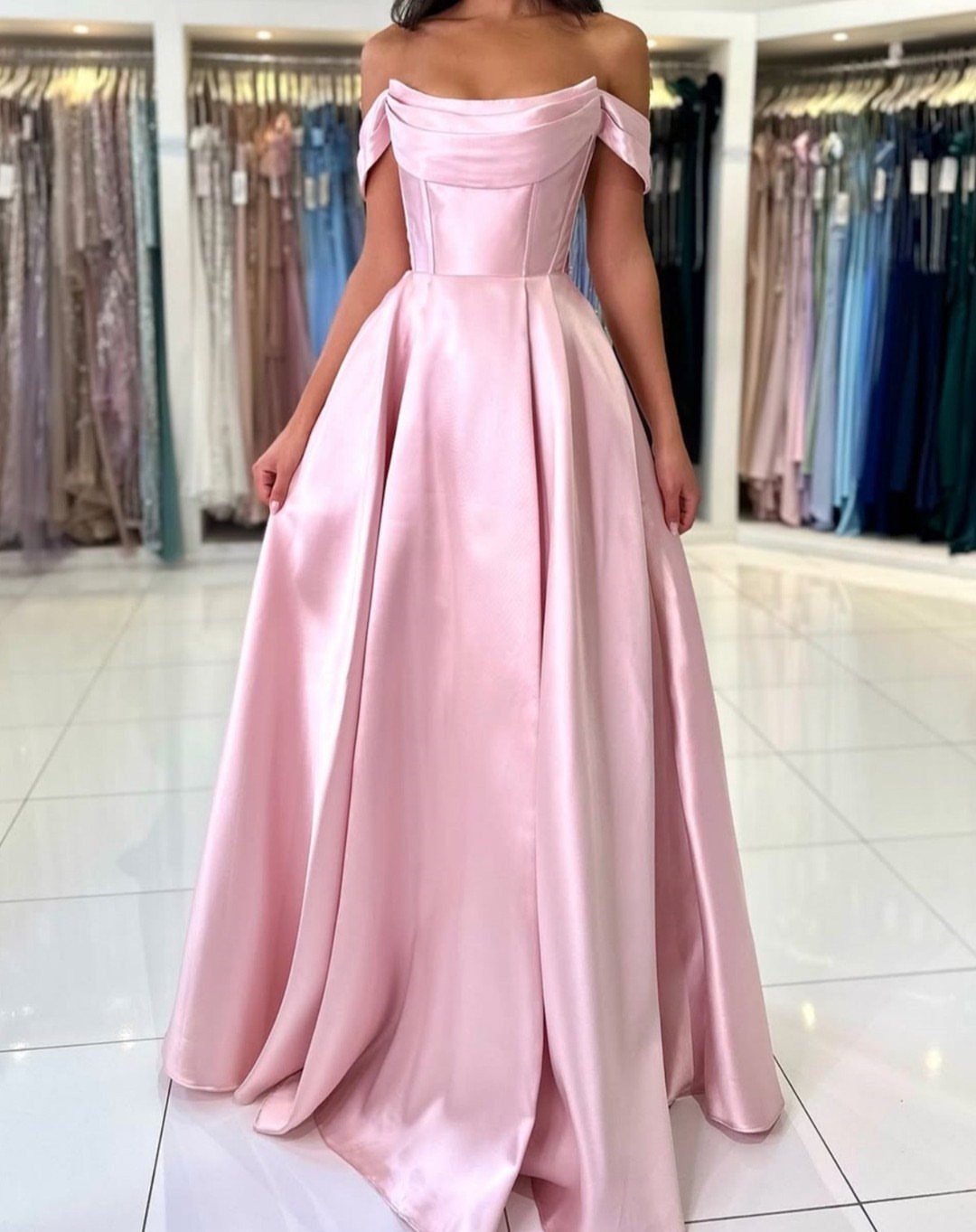 A woman posing in a floor-length, off-the-shoulder pink satin prom gown.
