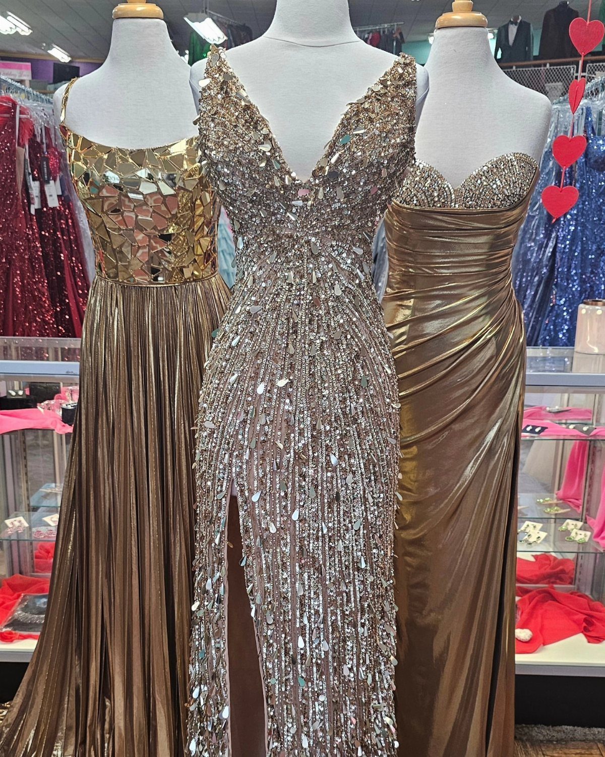 Three mannequins wearing sparkling gold and silver formal gowns in a boutique setting.