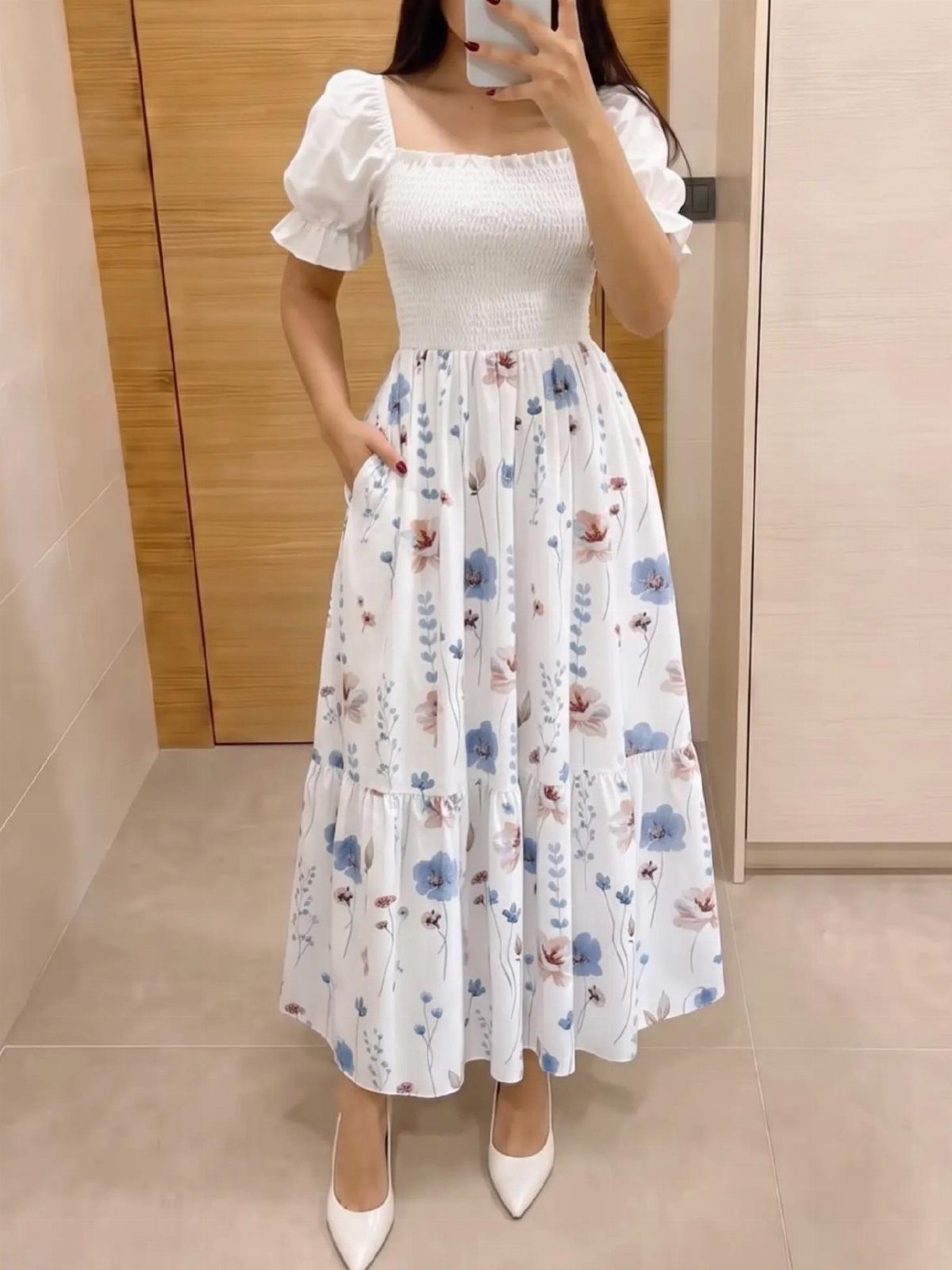 Woman wearing a white floral midi dress with blue and pink flower patterns.