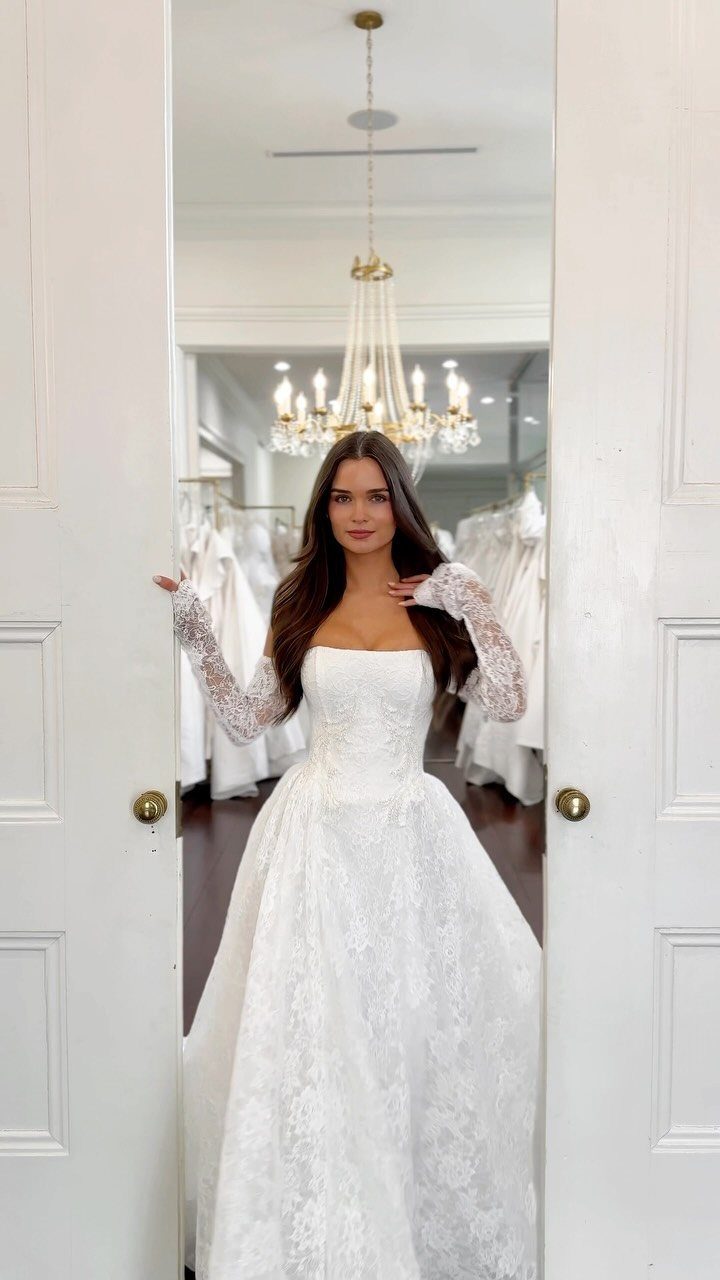 A woman wearing a white lace wedding dress with long sleeves posing in a doorway.