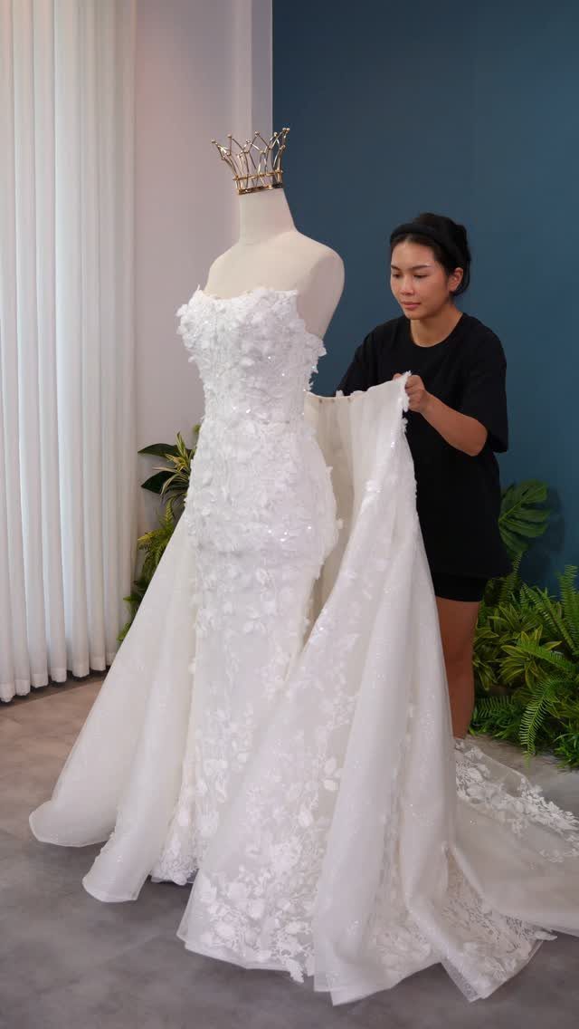 A white lace mermaid wedding dress being adjusted by a woman on a mannequin.