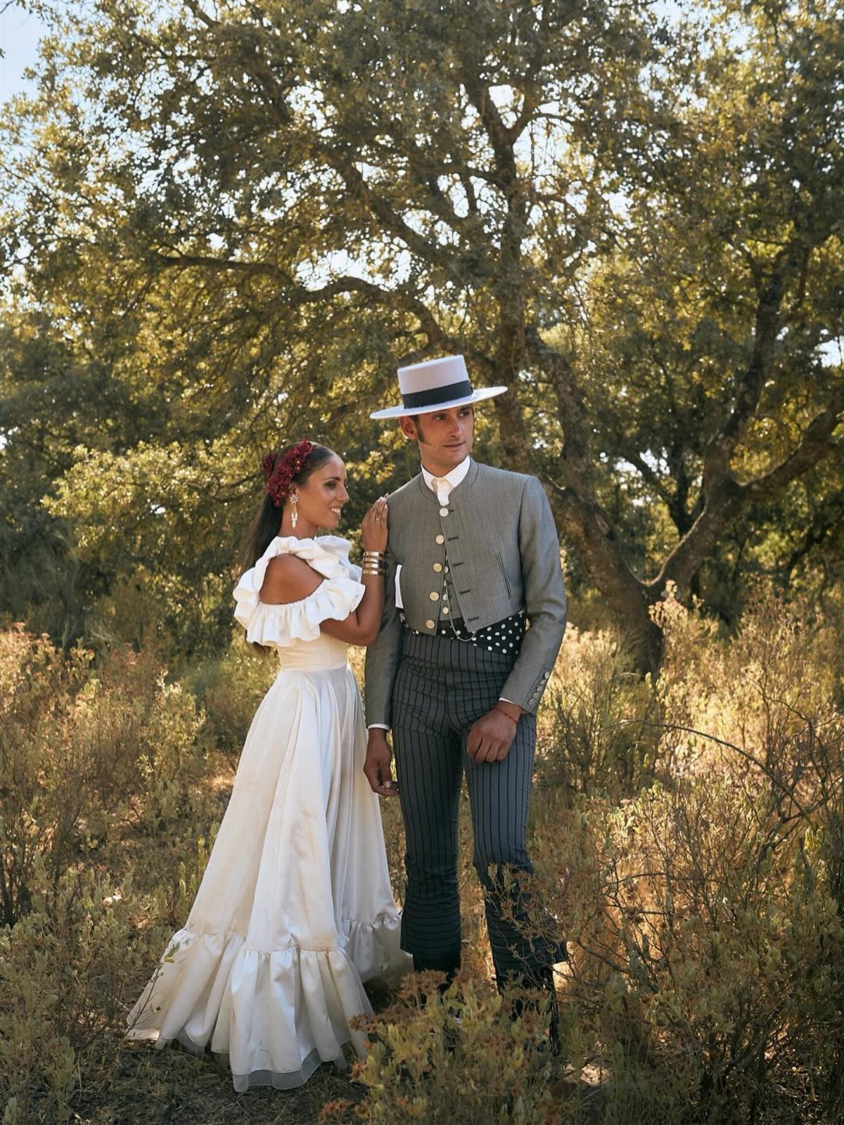 A woman in a white ruffled dress and a man in a boater hat posing in a field.