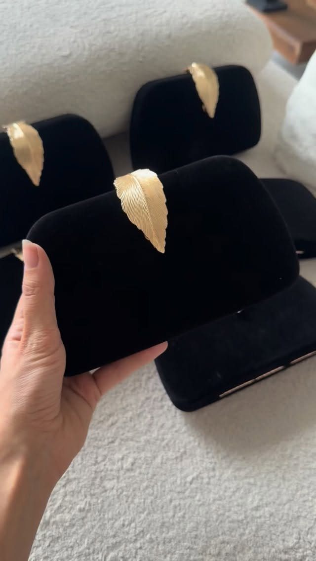 A hand holding a black velvet clutch decorated with a gold leaf ornament.