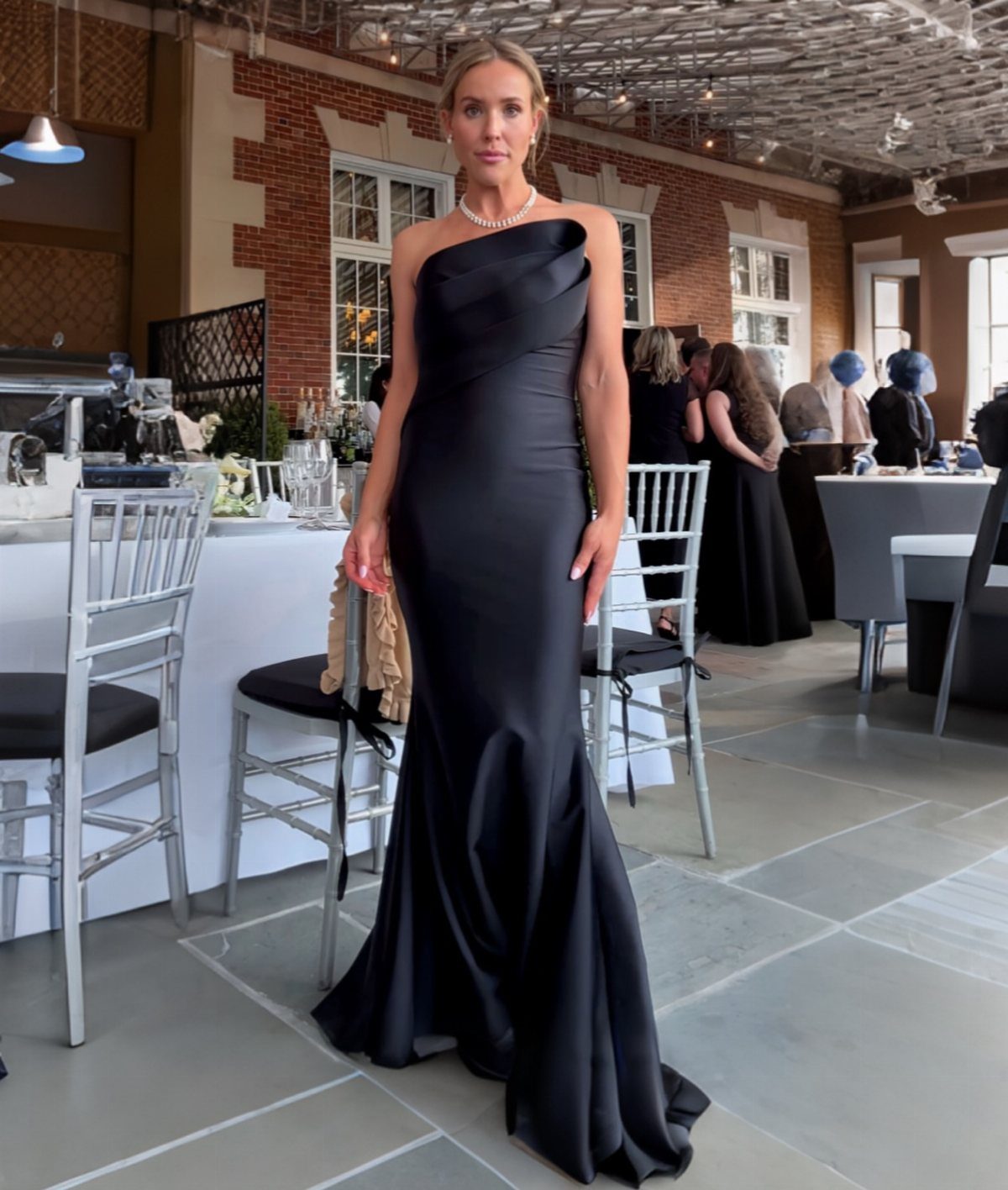 Woman in a black strapless floor-length satin gown standing in a formal banquet hall.