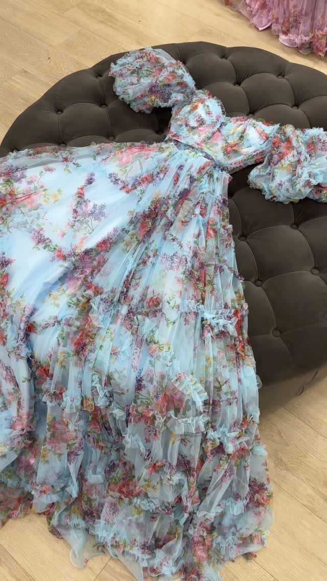 A light blue floral tulle gown with voluminous ruffles laid on a brown tufted ottoman.