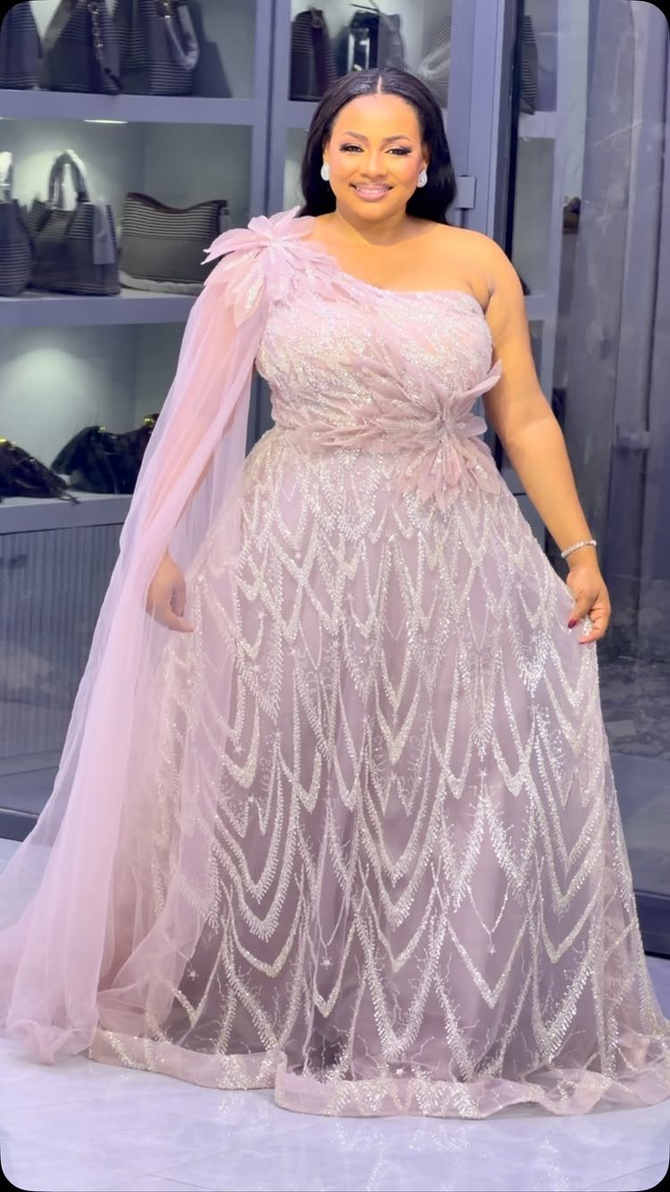 A woman smiling while wearing a shimmering pink one-shoulder gown with a tulle cape.