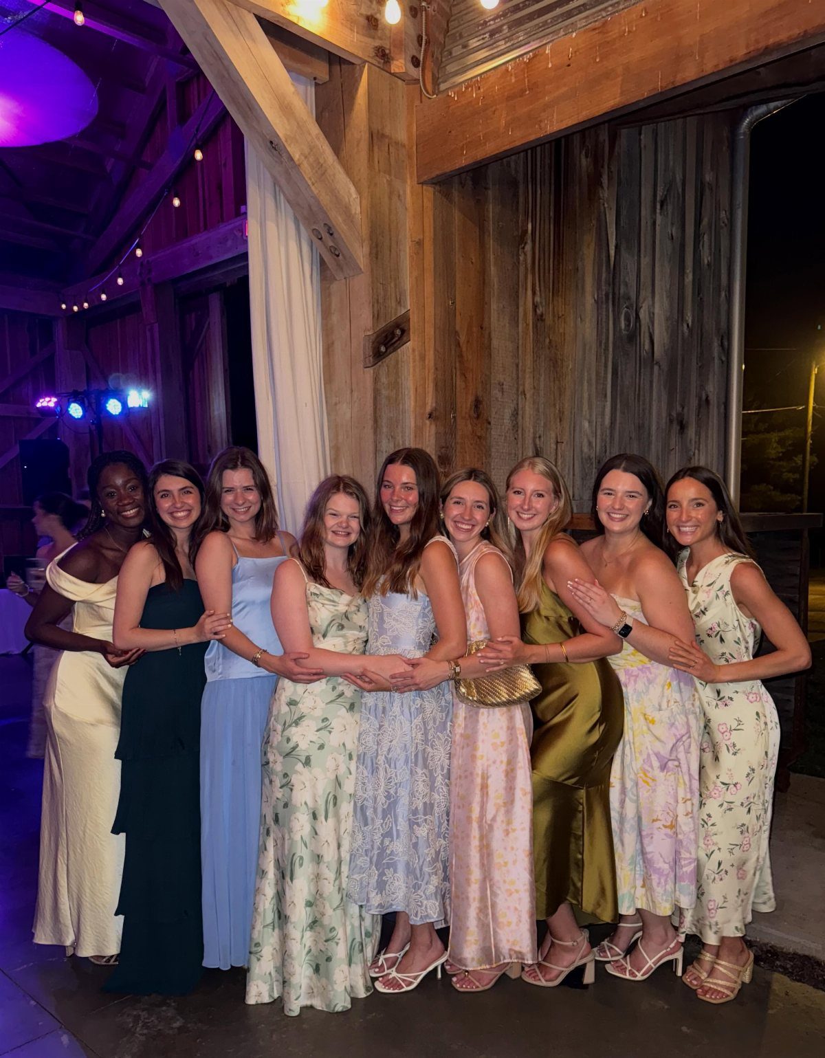 Nine young women posing together wearing various colorful spring dresses.