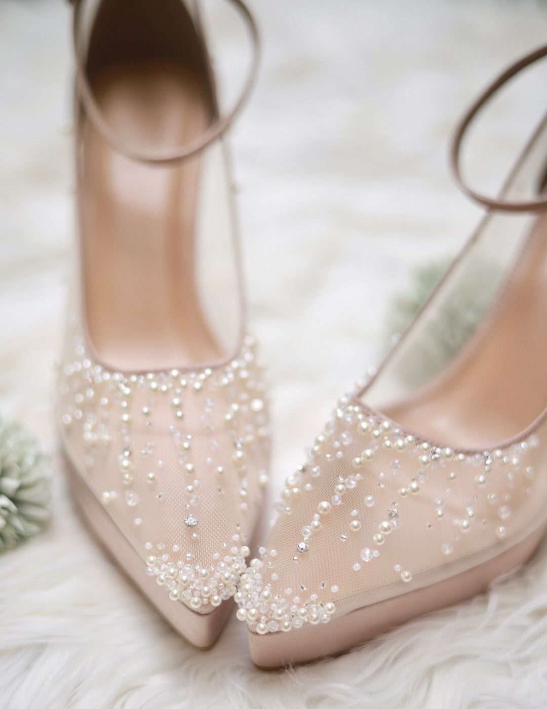 Pointed-toe mesh high heels decorated with pearls and crystals resting on white faux fur.
