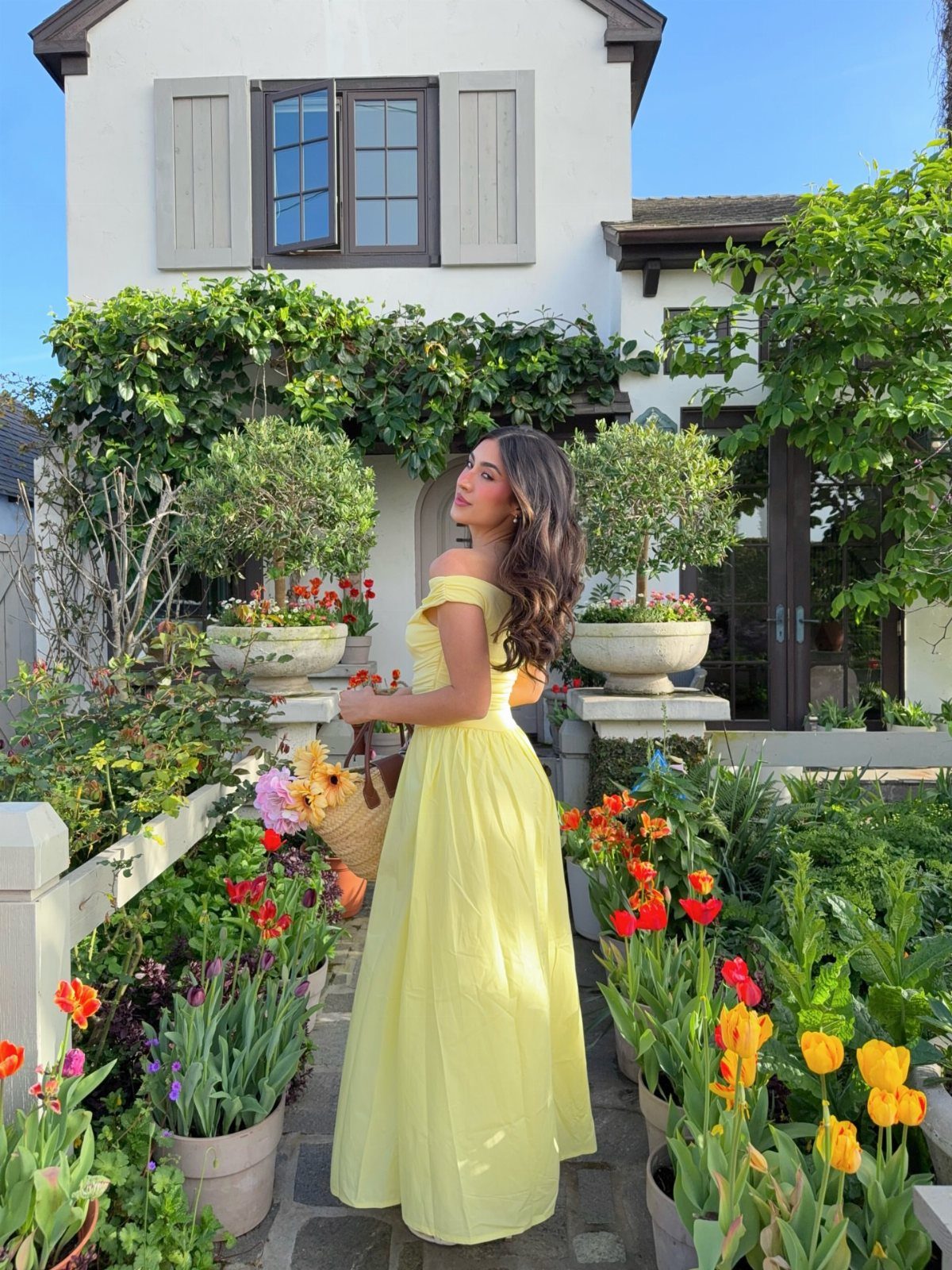 A woman wearing a long yellow sundress posing in a vibrant garden with colorful tulips.