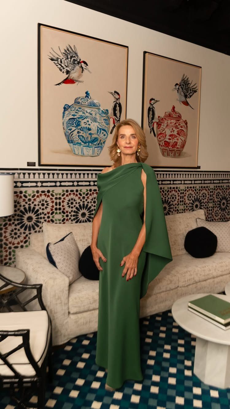 Older woman posing in a long emerald green cape-style gown in a decorated room.