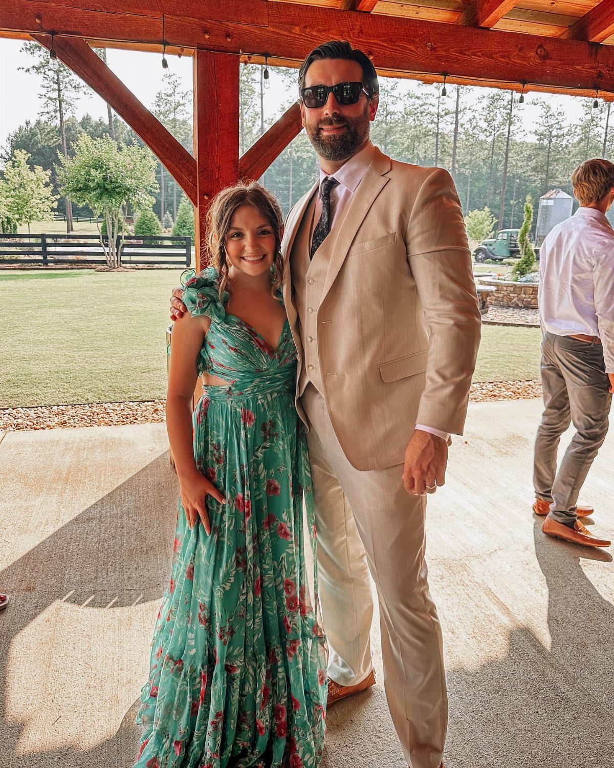 A man in a tan suit and a girl in a teal floral dress posing outdoors.