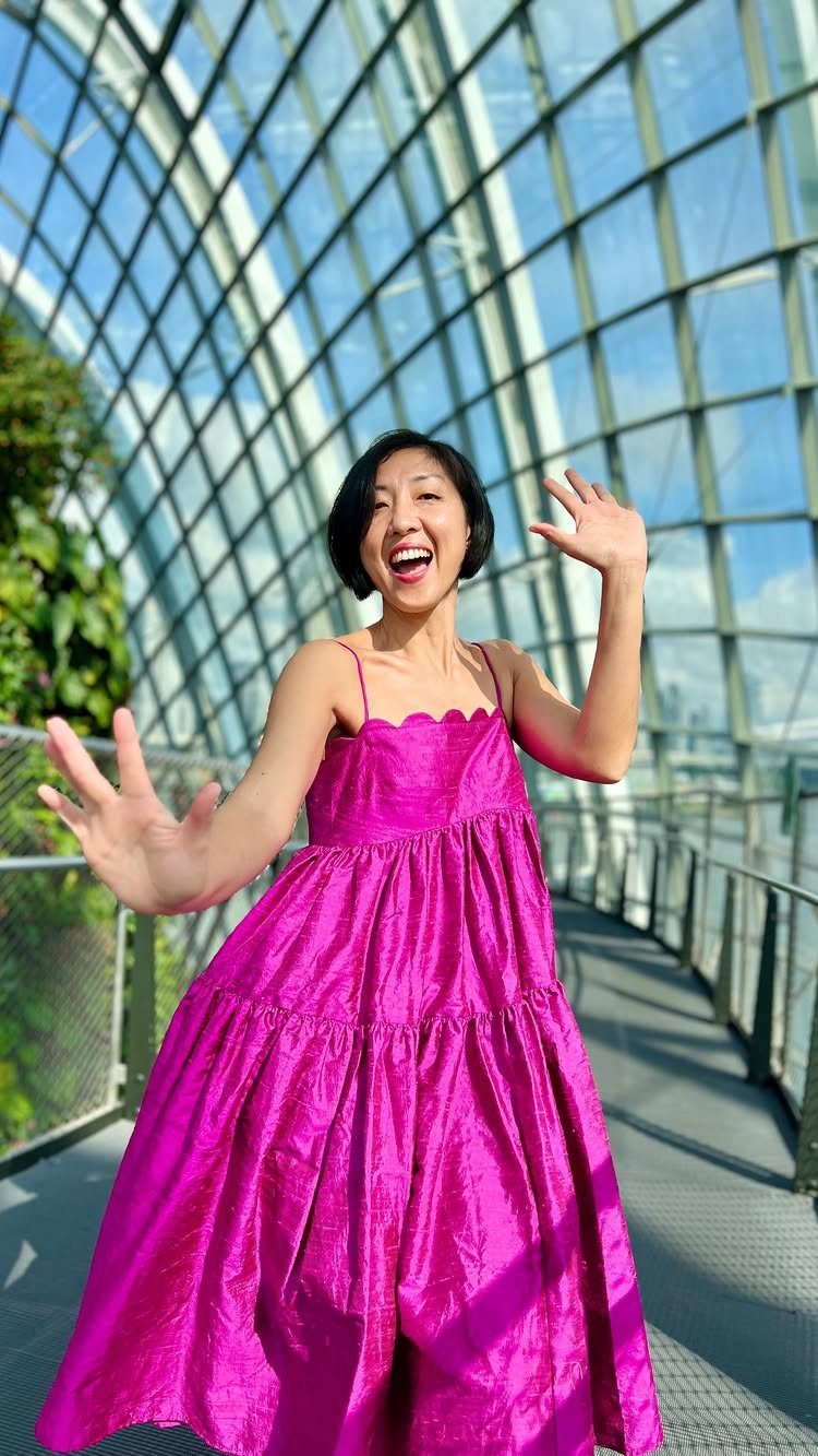 A woman in a bright pink babydoll dress smiling under a large glass dome structure.