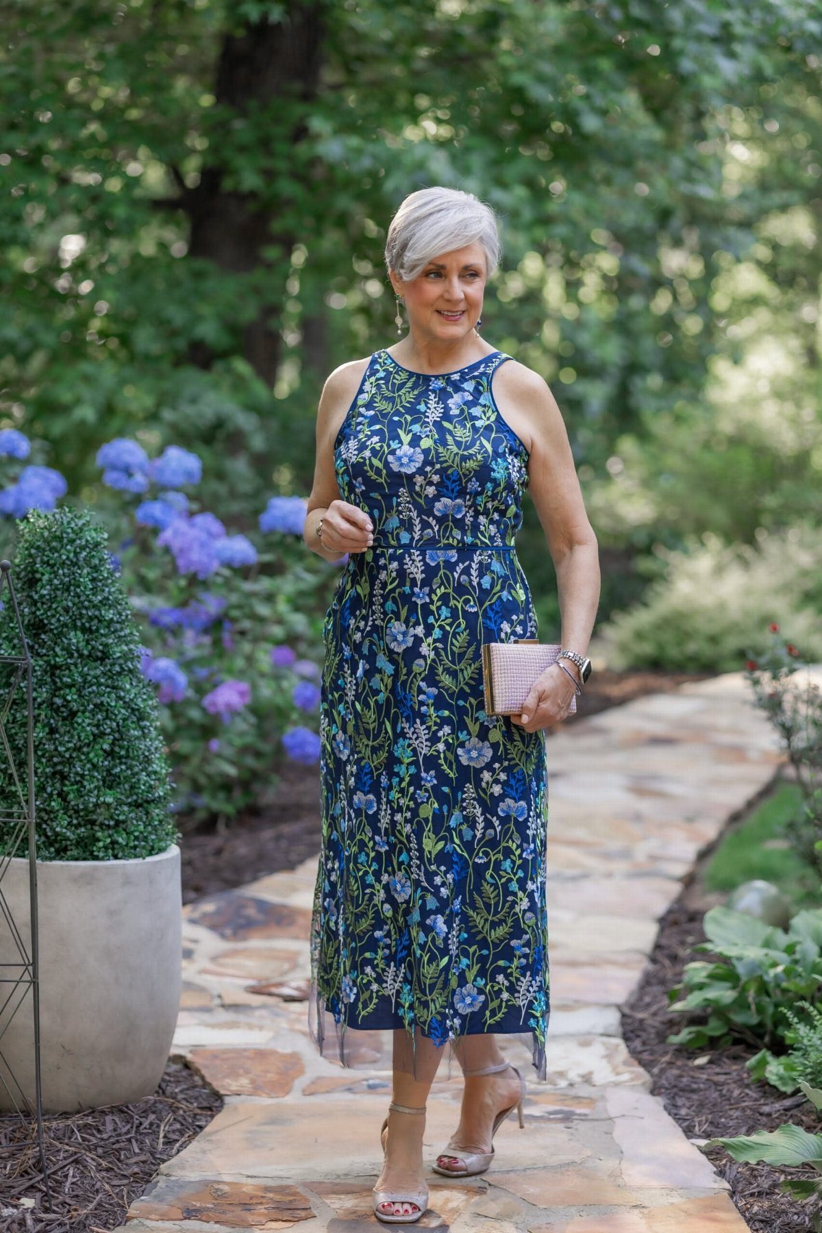Mature woman in a navy blue floral A-line midi dress standing in a garden.
