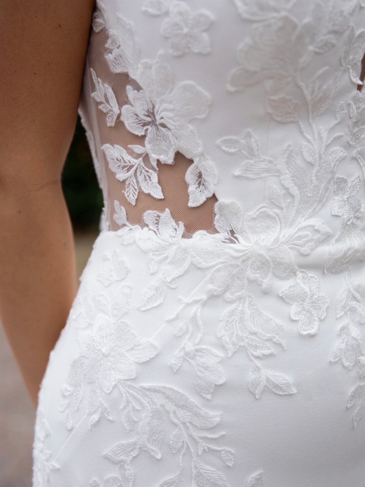 White wedding dress with intricate floral lace appliqués and sheer mesh detailing.