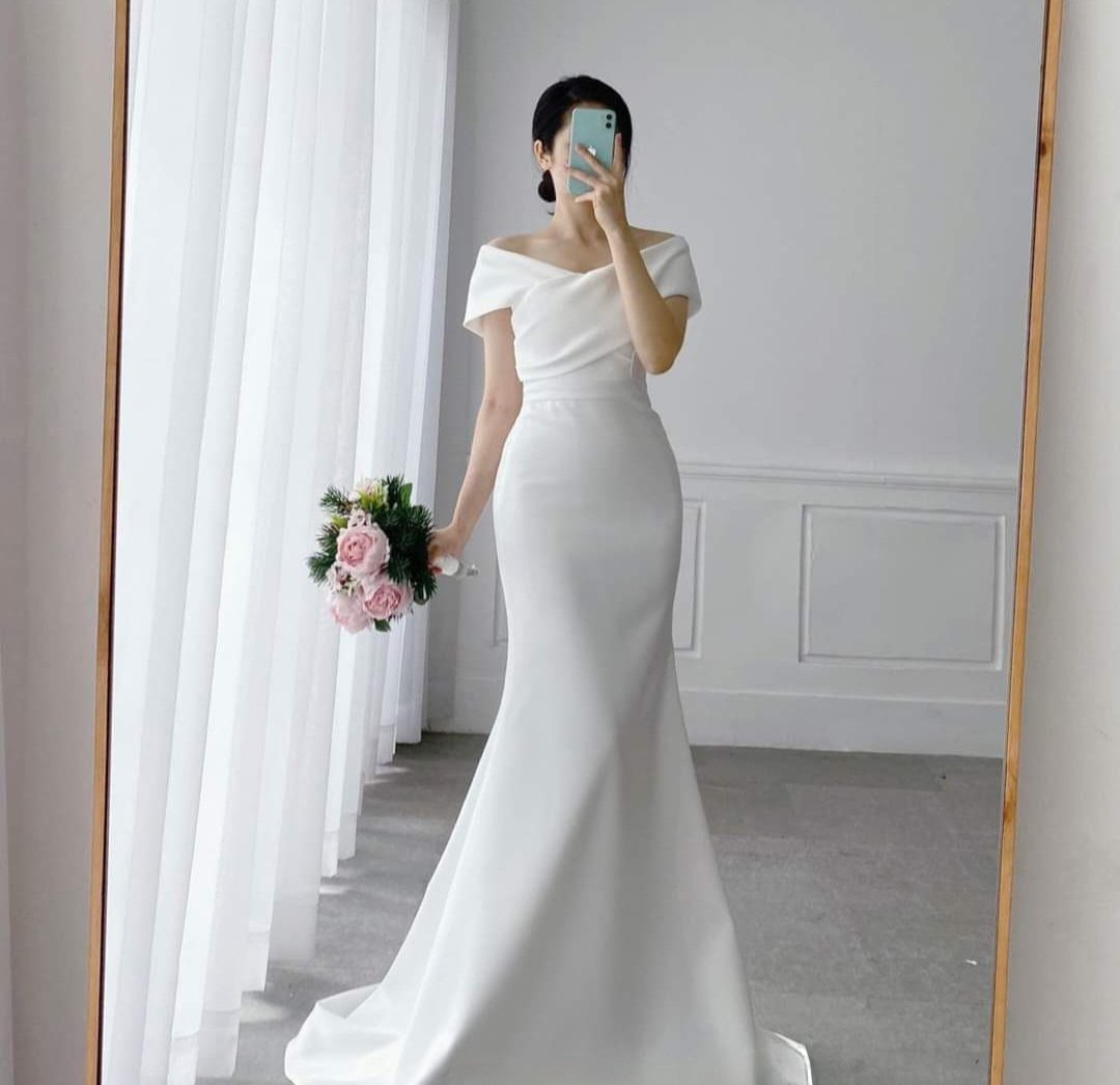 Woman in a white off-the-shoulder satin wedding gown holding a pink rose bouquet.