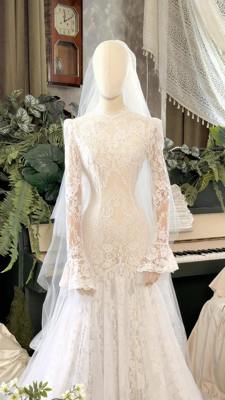 Lace mermaid wedding dress with long flared sleeves and a long veil on a mannequin.