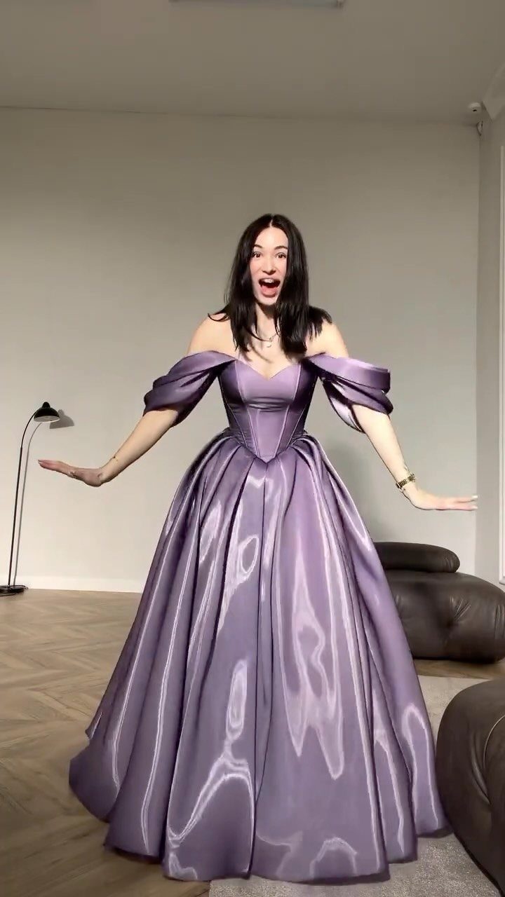 Woman wearing a voluminous lavender off-the-shoulder ball gown in a bright room.