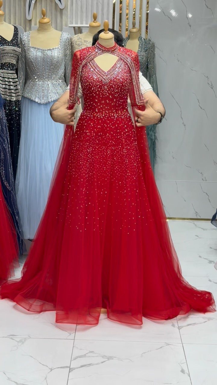 Red beaded gown with a sheer cape overlay displayed on a mannequin.