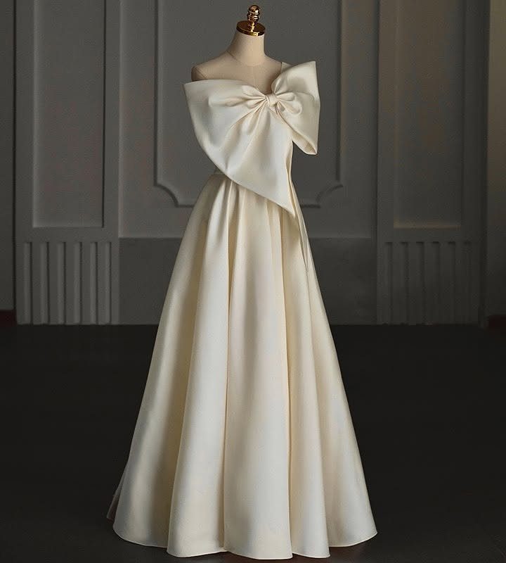 Cream satin strapless gown with a large decorative bow on a mannequin.