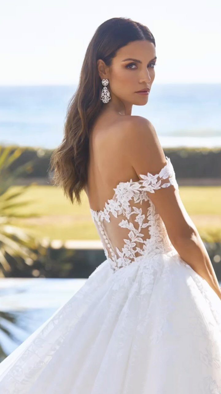 Woman wearing a white lace off-the-shoulder wedding gown posing by the ocean.