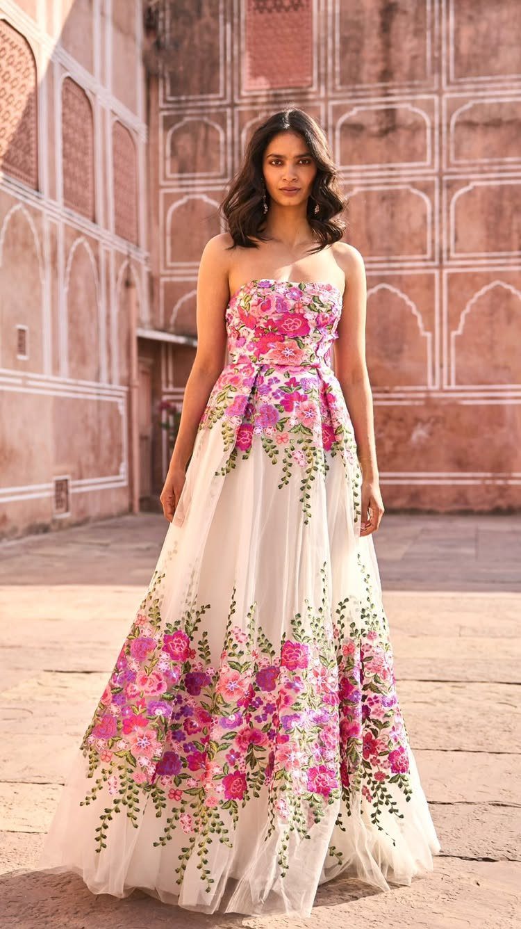 A woman poses in a white strapless gown with colorful pink and purple floral embroidery.