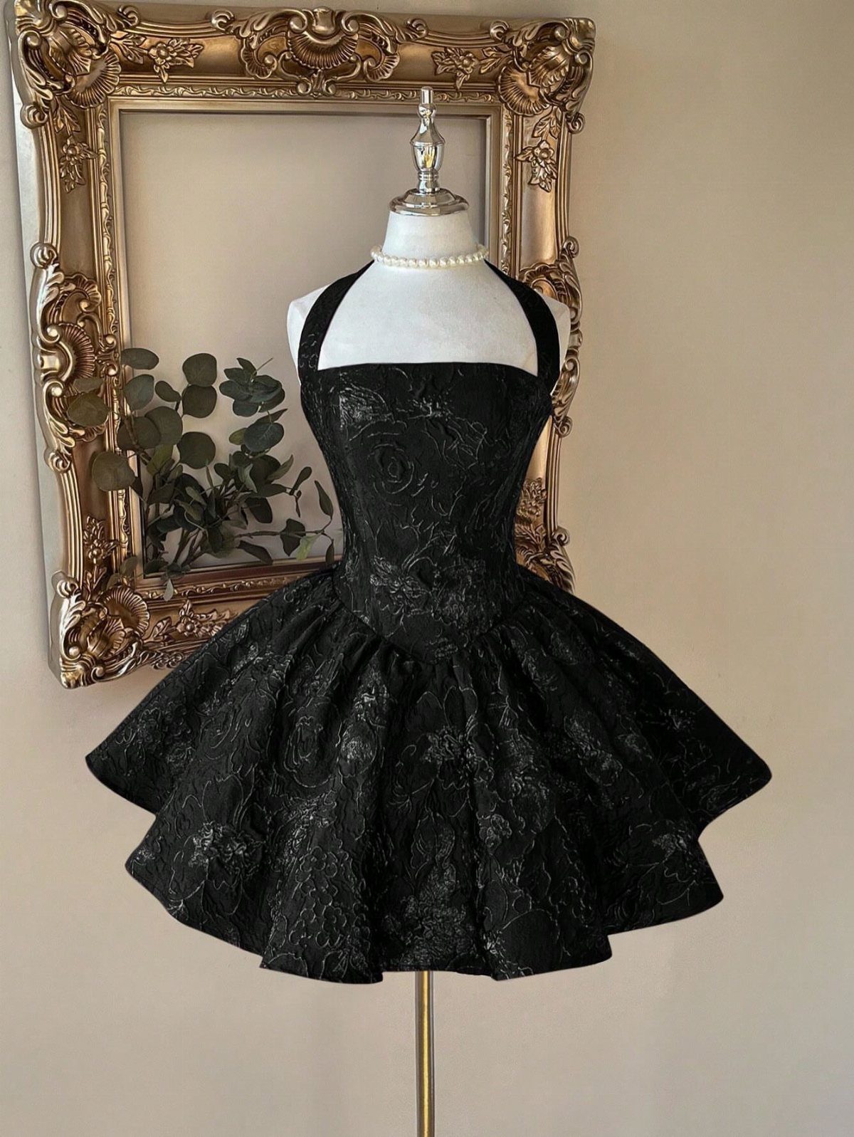 Black halter mini dress with a voluminous flared skirt displayed on a white mannequin.
