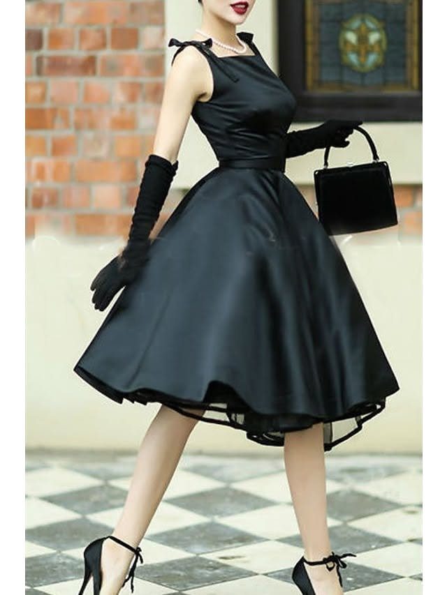 Woman in a black satin A-line dress wearing long black gloves and holding a small handbag.