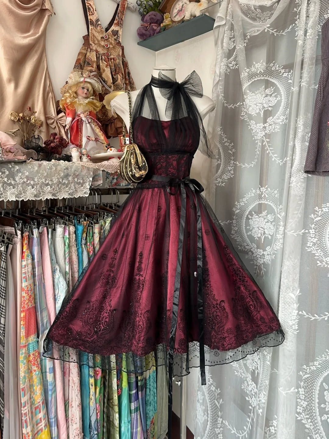 Burgundy satin A-line dress with black lace detailing and a sheer bow displayed on a mannequin.