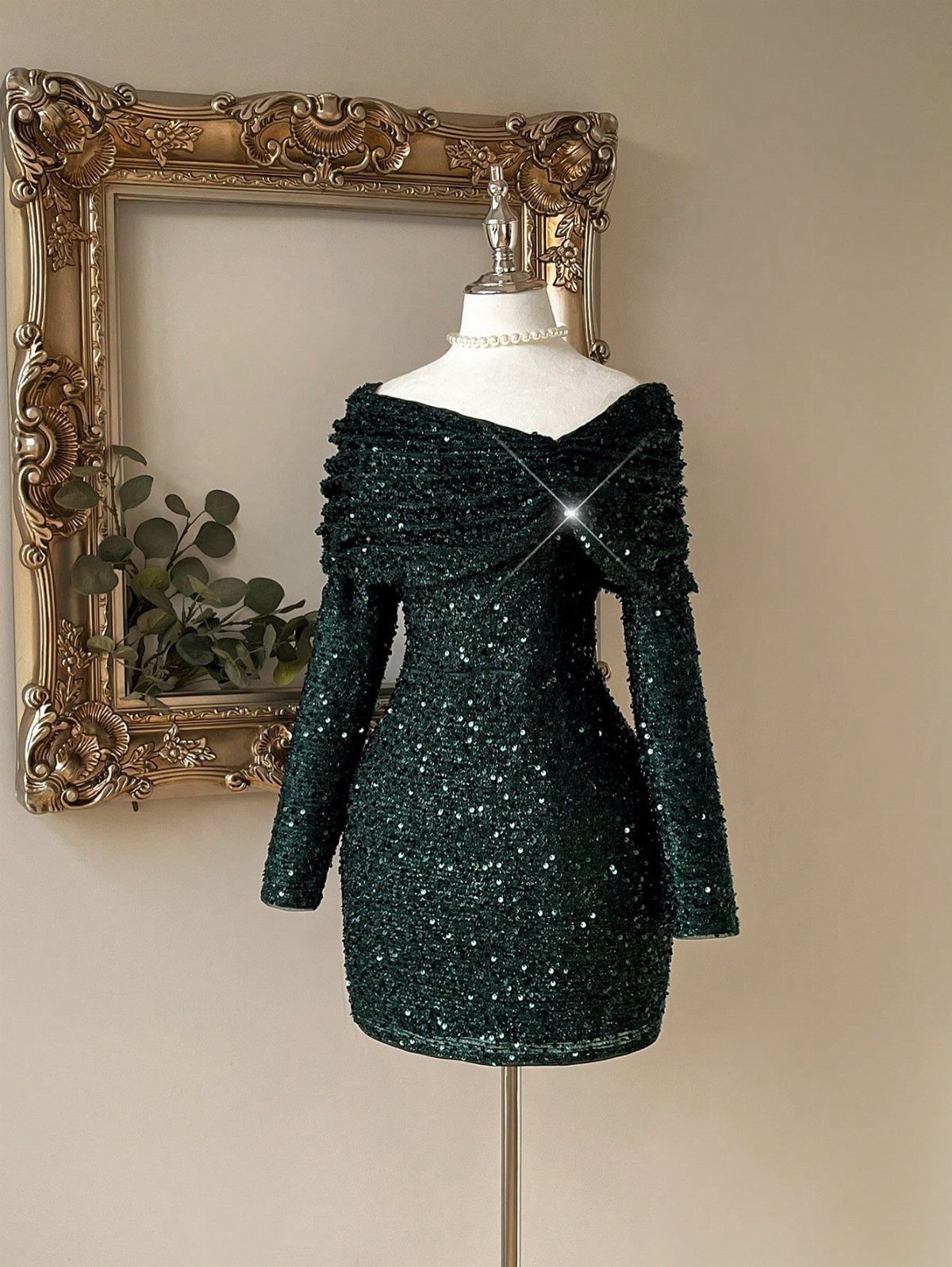 Dark green sequined off-the-shoulder mini dress displayed on a white mannequin against a neutral wall.