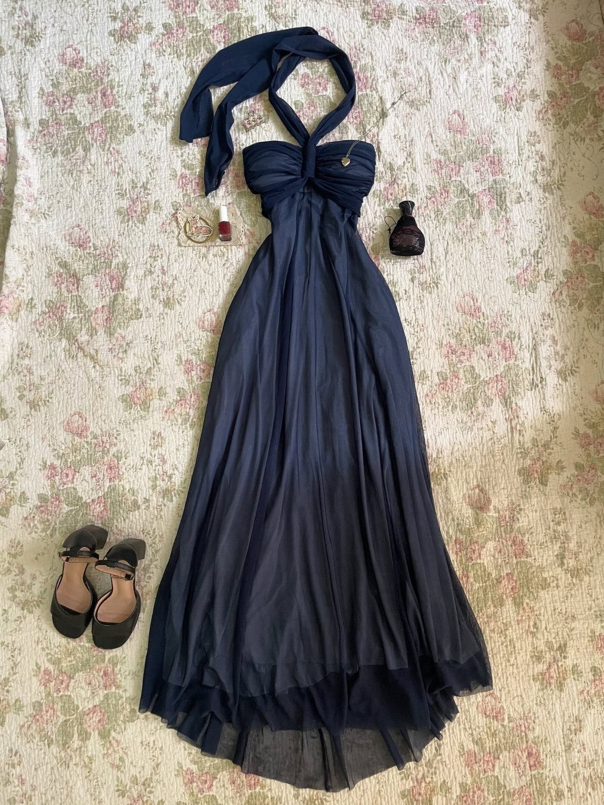 Navy blue halter maxi dress with a flowing skirt laid on a floral patterned fabric with black heels.