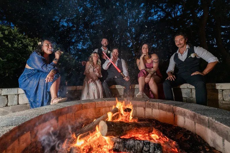 People relaxing around a glowing stone fire pit during a nighttime outdoor gathering.