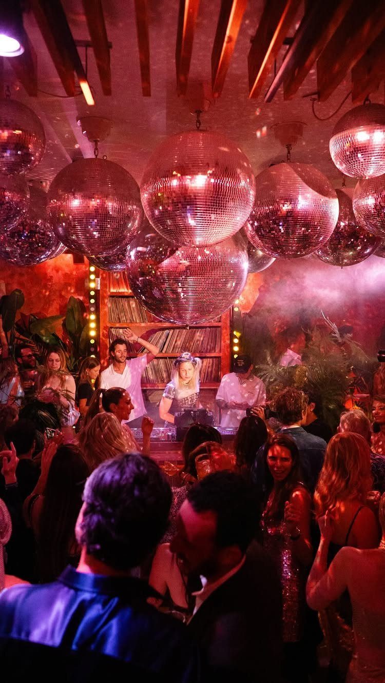 Crowd of people dancing in a dimly lit club under large sparkling disco balls.