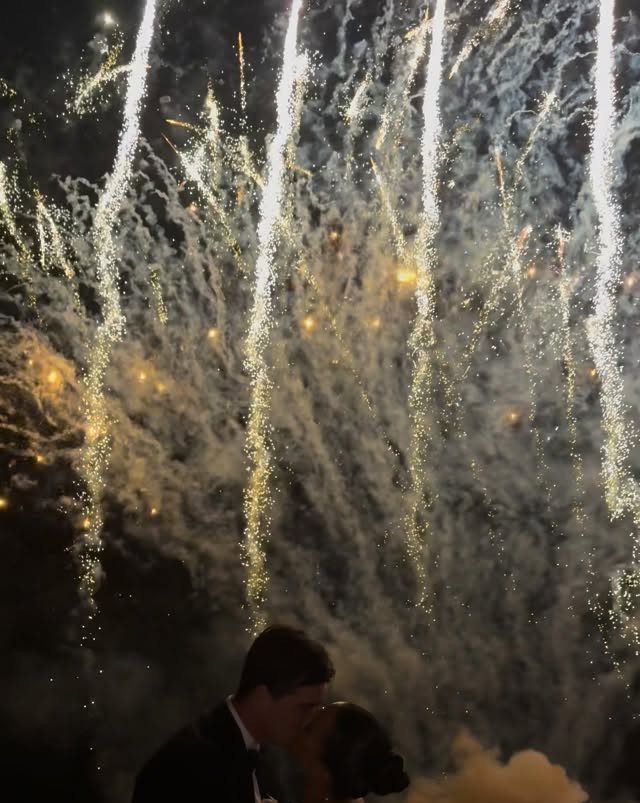 A couple silhouettes kissing under a spectacular display of golden and white fireworks.